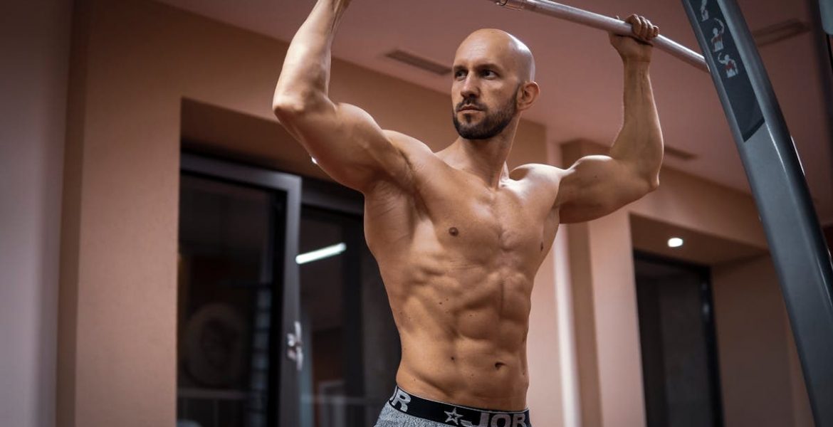 A bald, muscular man performing exercise on gym equipment indoors.
