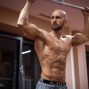 A bald, muscular man performing exercise on gym equipment indoors.